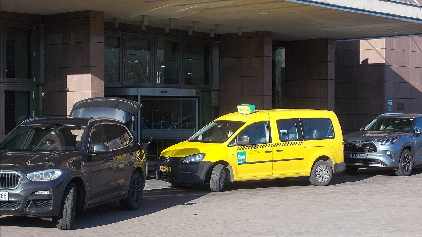 A yellow licensed Budapest taxi with a Bolt Taxi roof sign and Bolt logo, parked outside a hotel entrance