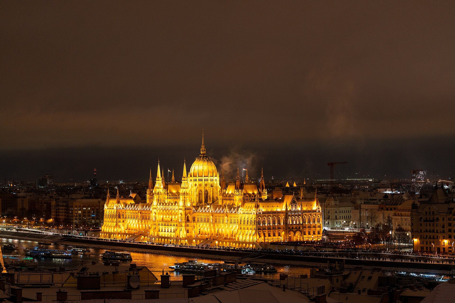 The Hungarian Parliament lit up at night across the Danube, seen over snow-covered rooftops in Buda