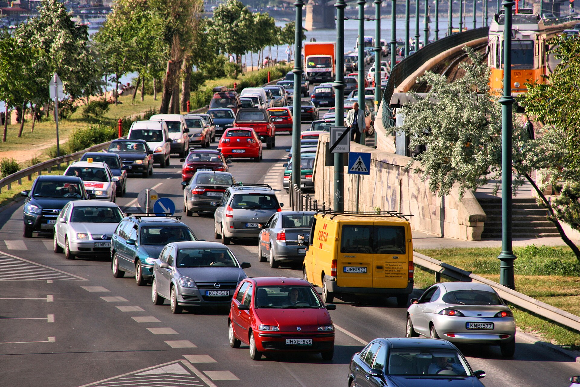 Heavy traffic congestion on a Budapest street beside the Danube, with a tram passing on an elevated section