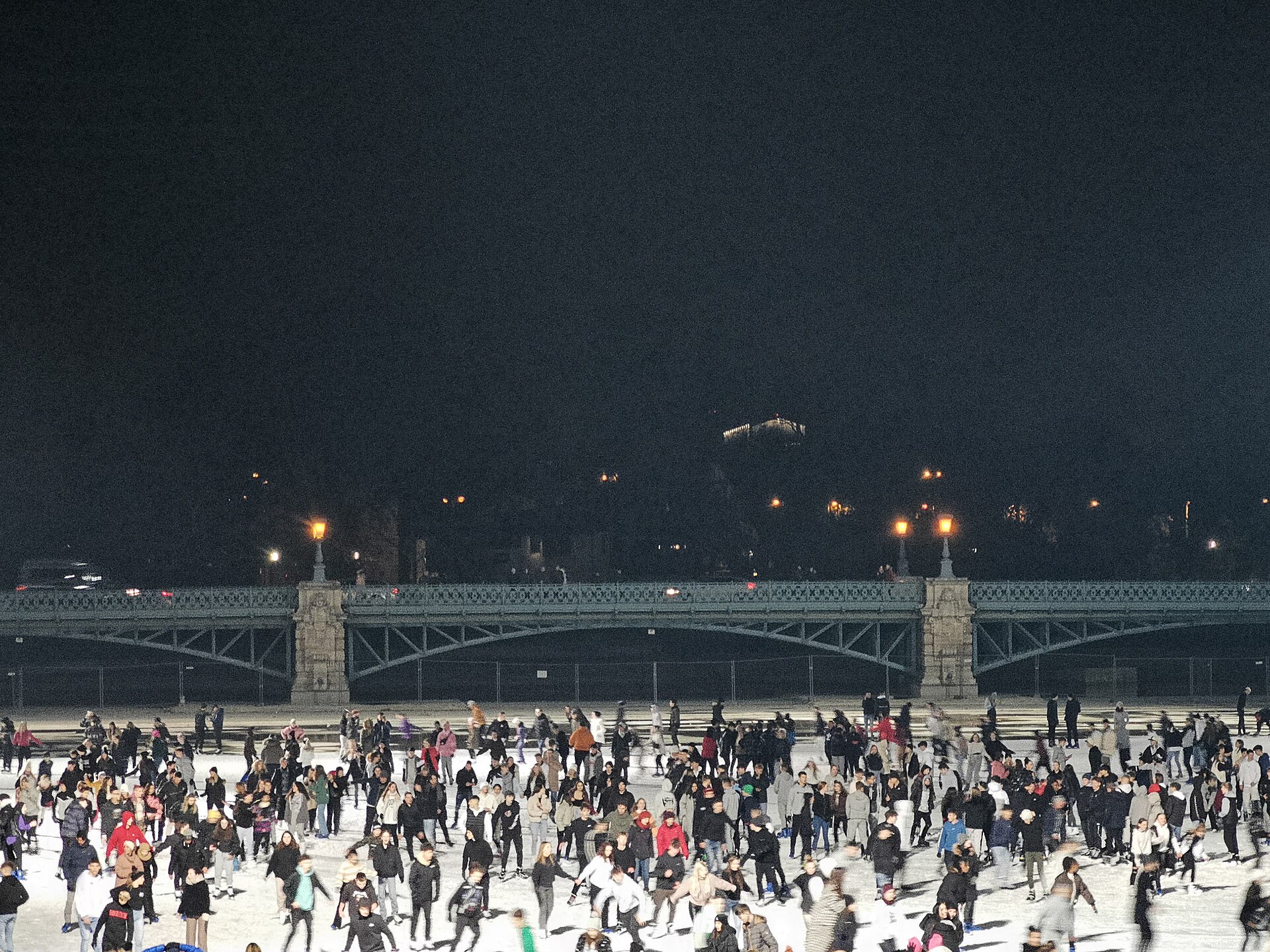 Crowds of skaters on the City Park Ice Rink at night, with a lit bridge and Vajdahunyad Castle behind