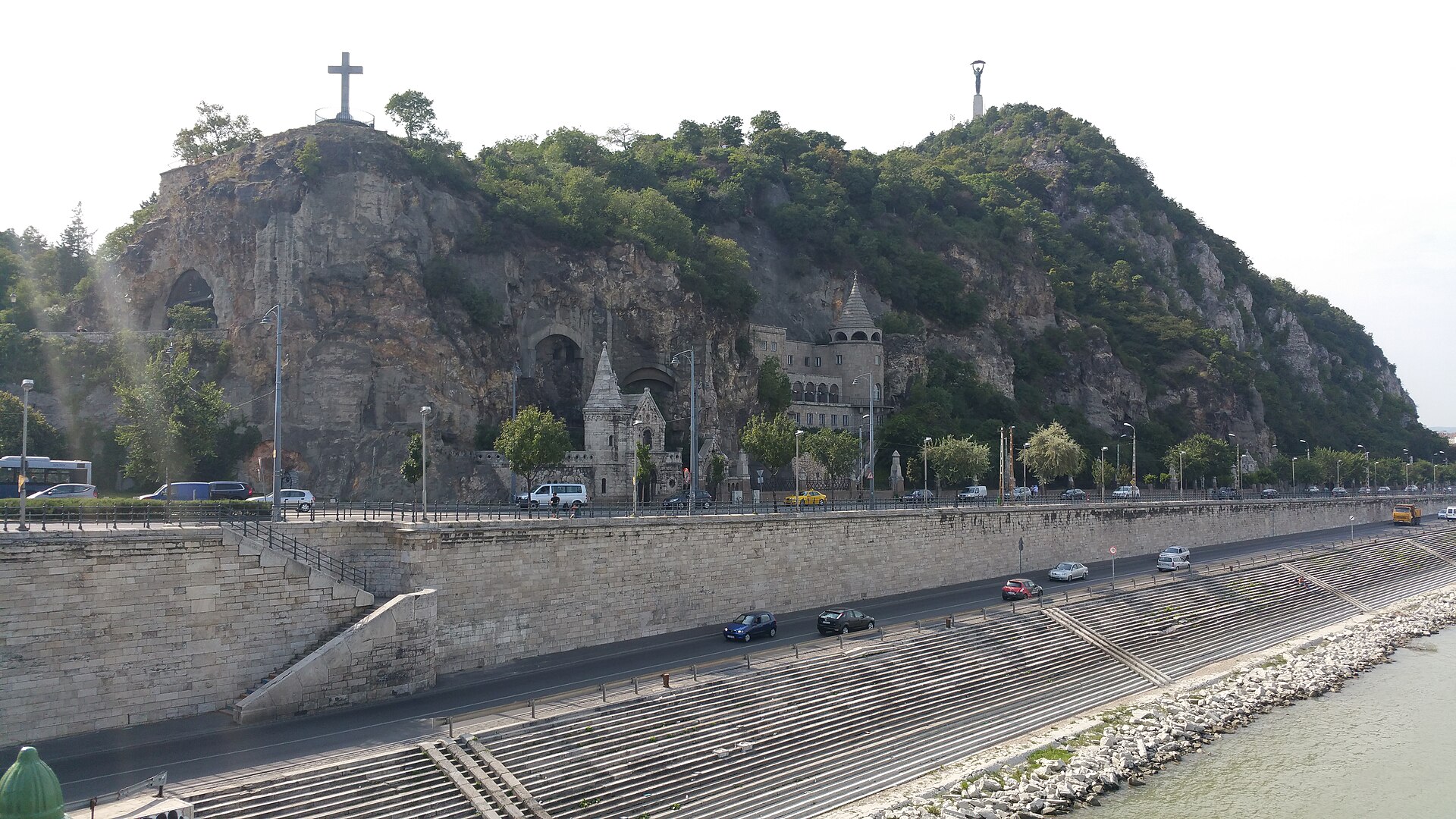 The rock face of Gellert Hill in Budapest showing the Cave Church entrance built into the cliff, with the Liberty Statue visible on the summit above