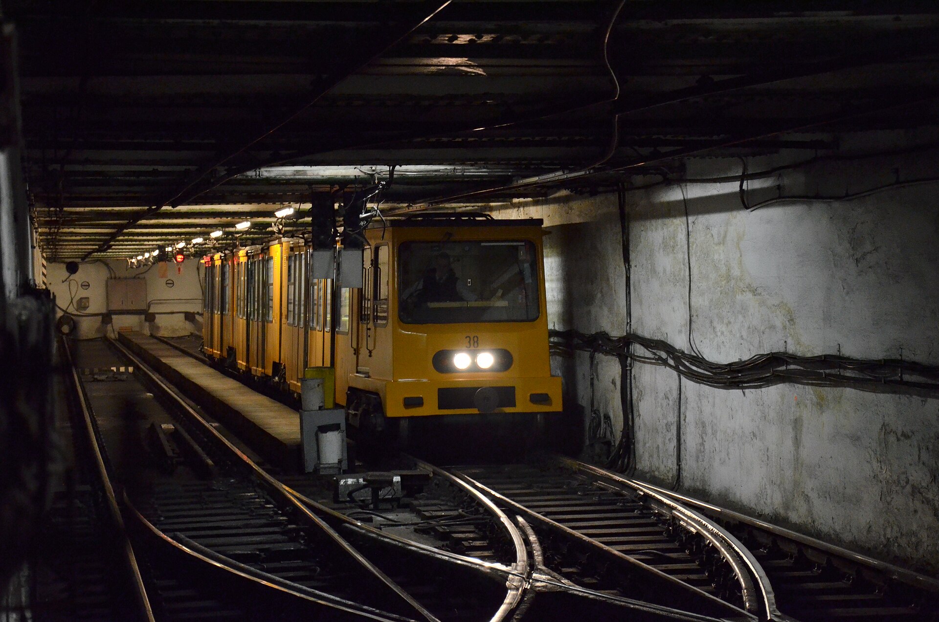 A small yellow historic M1 metro carriage in a Budapest tunnel, arriving at Vörösmarty tér station