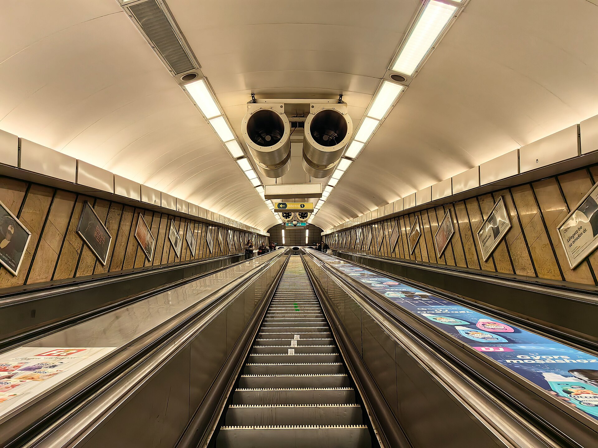 A long, steep escalator inside Deak Ferenc ter metro station in Budapest, descending toward the M2 platform
