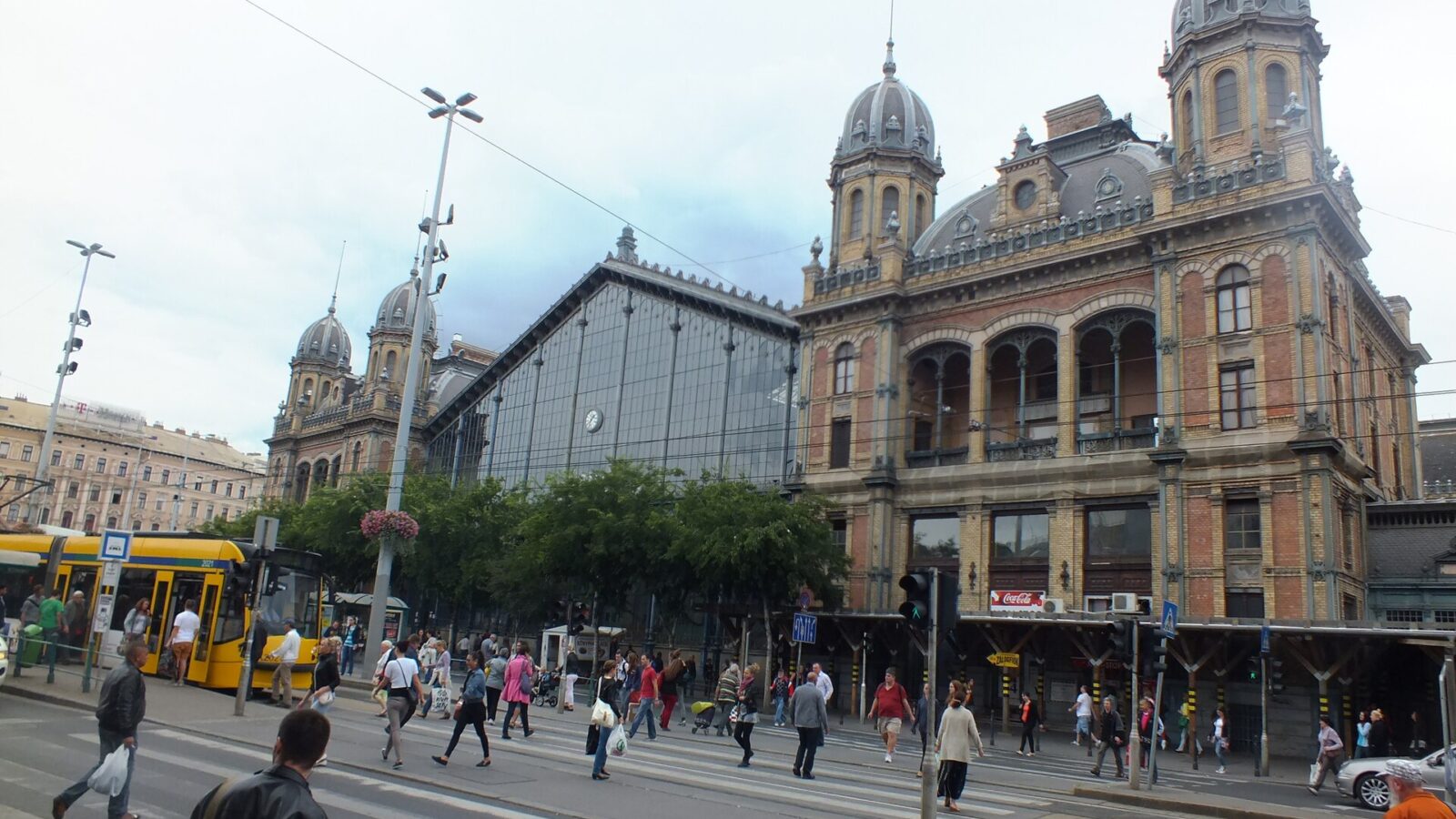 The ornate facade of Budapest's Nyugati railway station, with its iron-and-glass train shed and a yellow tram passing in front