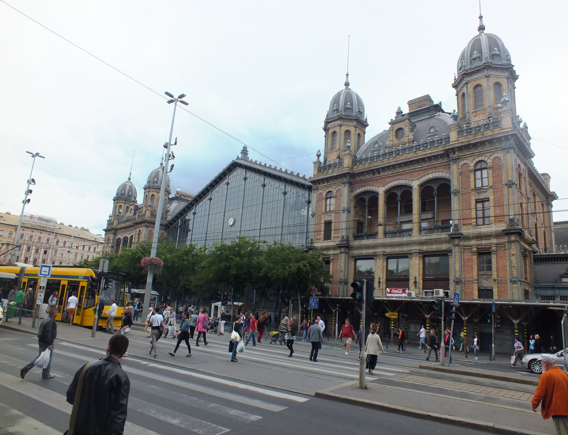 The iron-and-glass facade of Nyugati station with a tram passing in front
