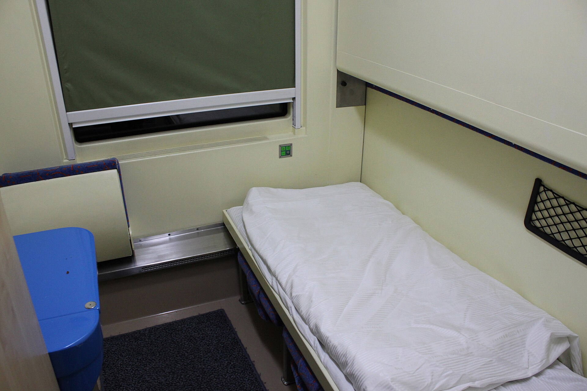 A compartment in a PKP Intercity sleeping car, with a made-up berth, a window blind and a fold-down washbasin cabinet