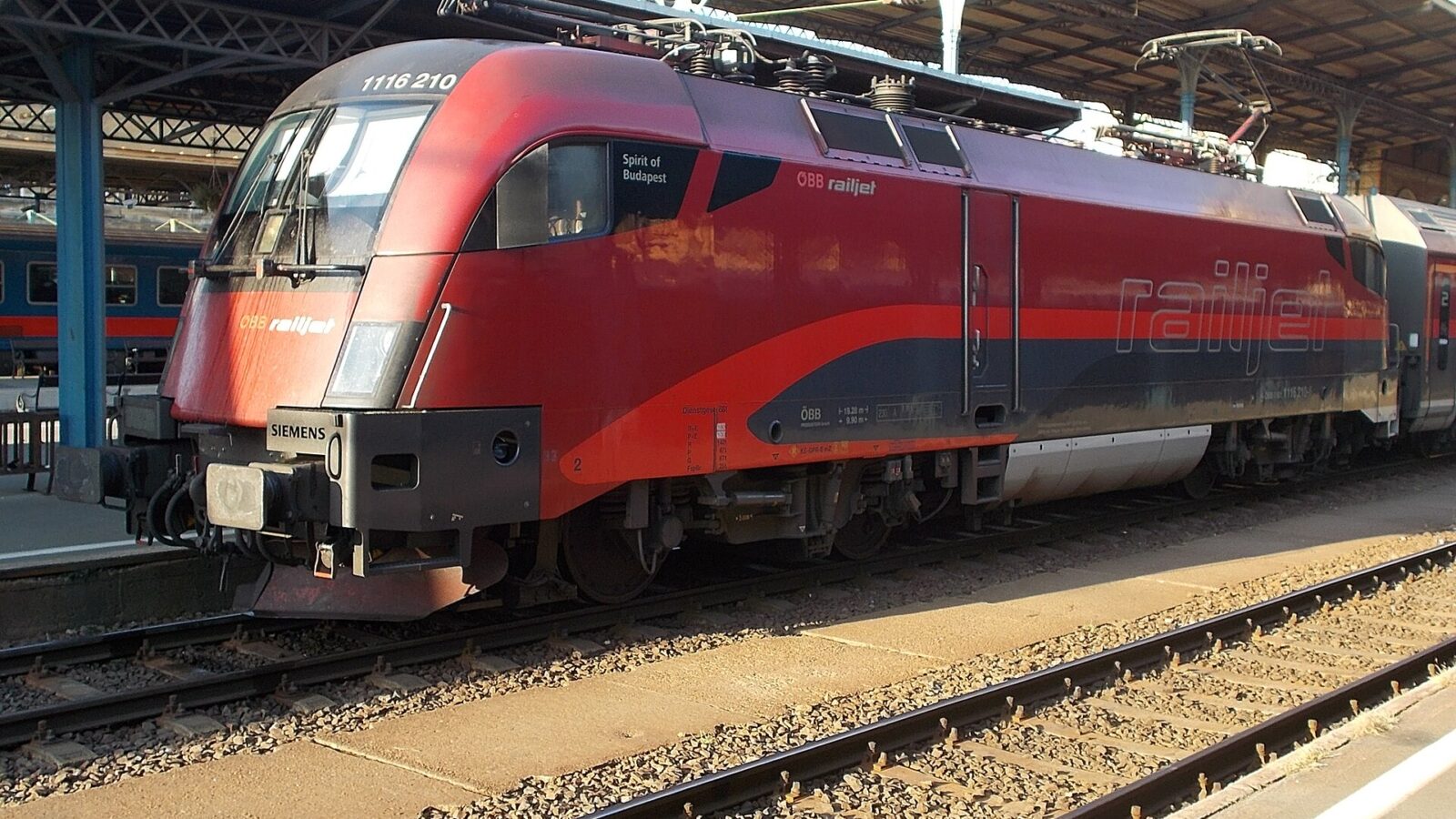 A red ÖBB Railjet locomotive named Spirit of Budapest waiting at a Budapest station platform