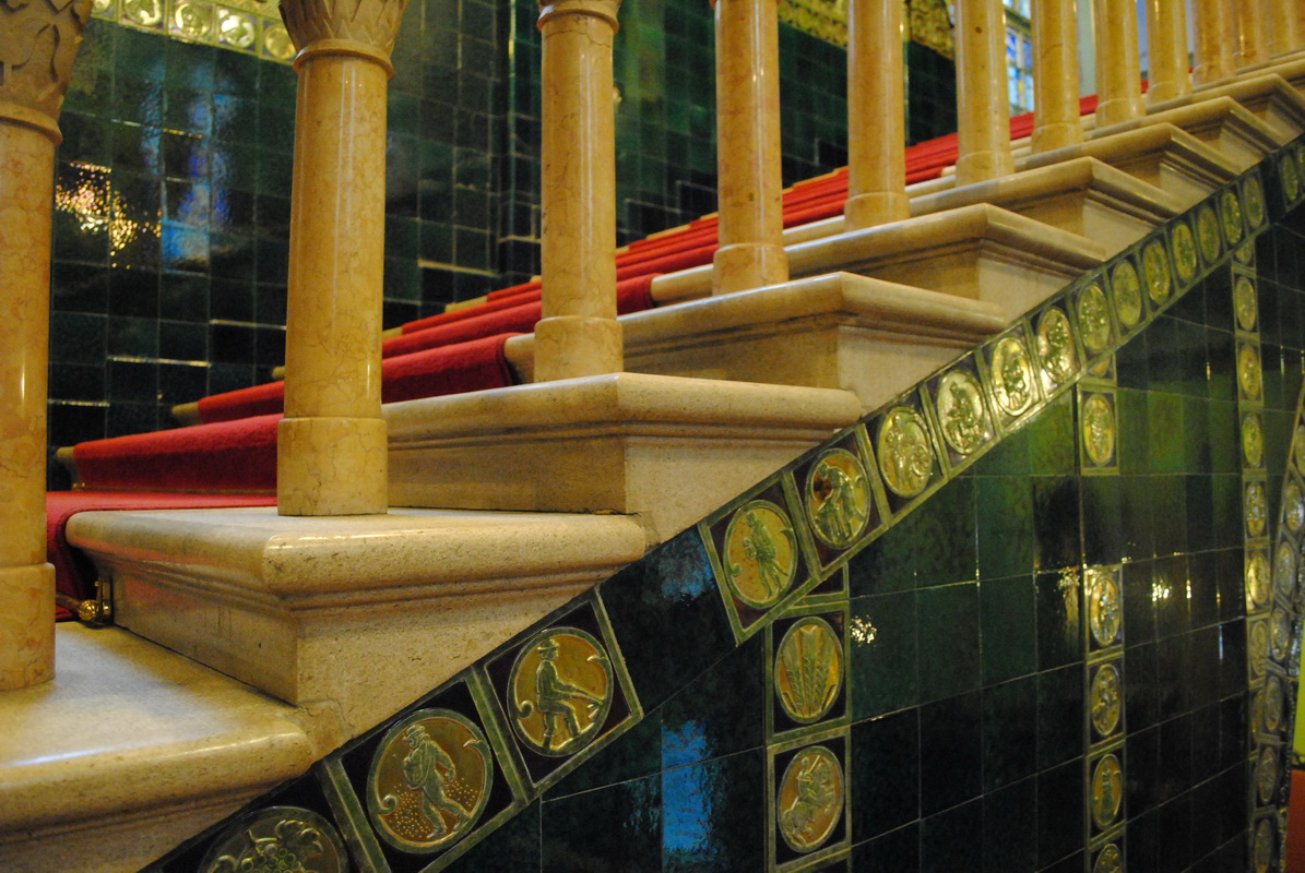 The grand staircase inside Subotica City Hall, lined with green Zsolnay ceramic tiles and gilded medallions, with a red carpet
